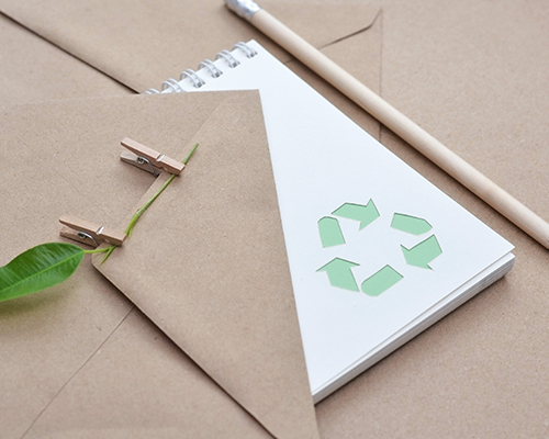 Ein Zeichenblock mit Recycling Logo, welcher auf Briefumschlägen liegt