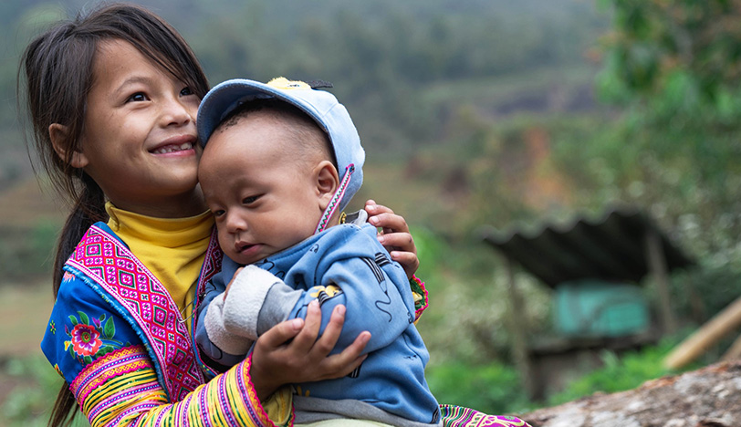 Ein lächelndes Mädchen hält einen kleinen Jungen im Arm.